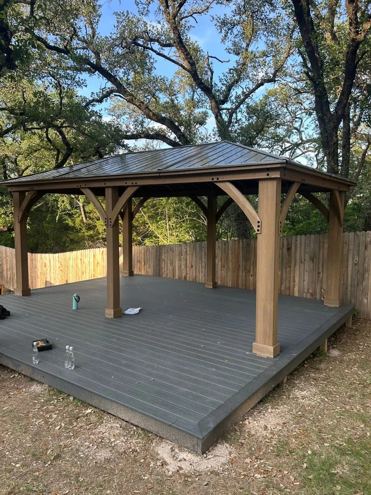 Wood gazebo with a metal roof standing on a newly built grey deck in a backyard